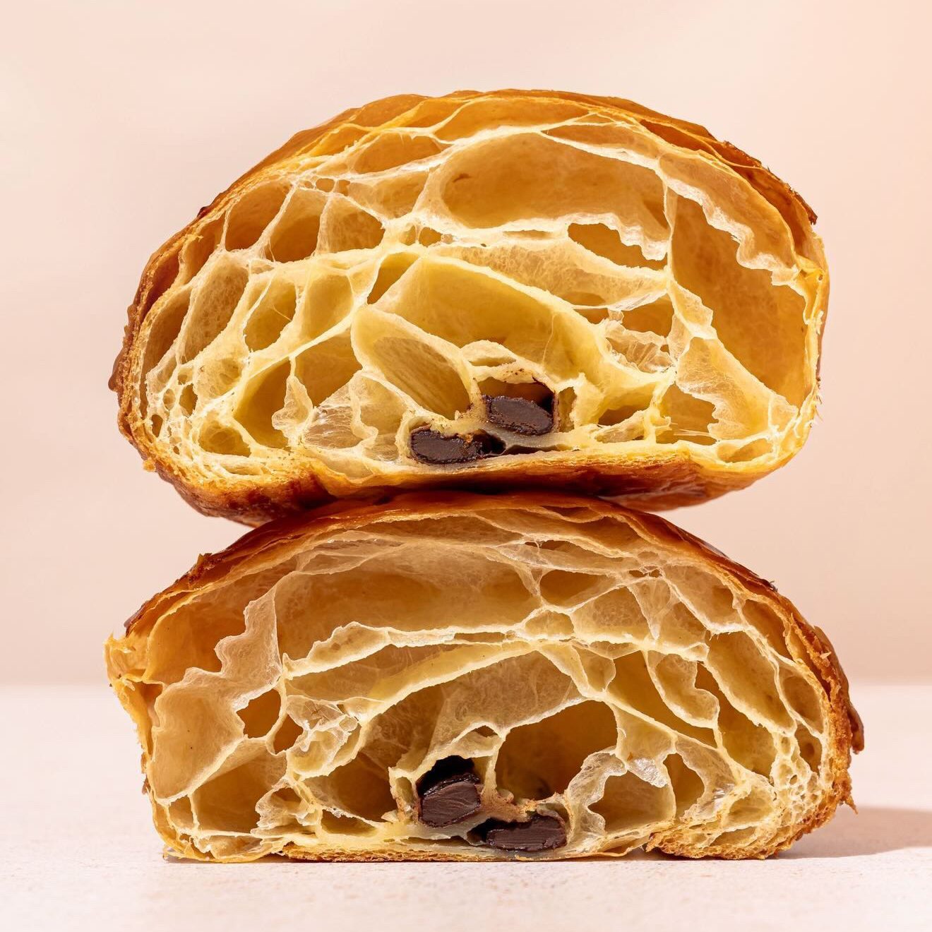 Jamie Sun_5 - IN München - Das Stadtmagazin Cross-section of a flaky croissant filled with dark chocolate chips, showing airy crumb and layers in a golden crust.