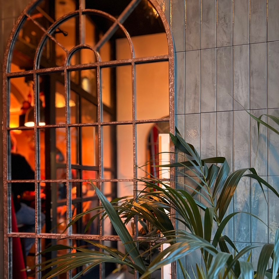 Martina Grandjean_1 - IN München - Das Stadtmagazin Rusty arched metal window grille with a green palm plant in the foreground; warm interior lighting visible through the bars and tiled wall on the right.