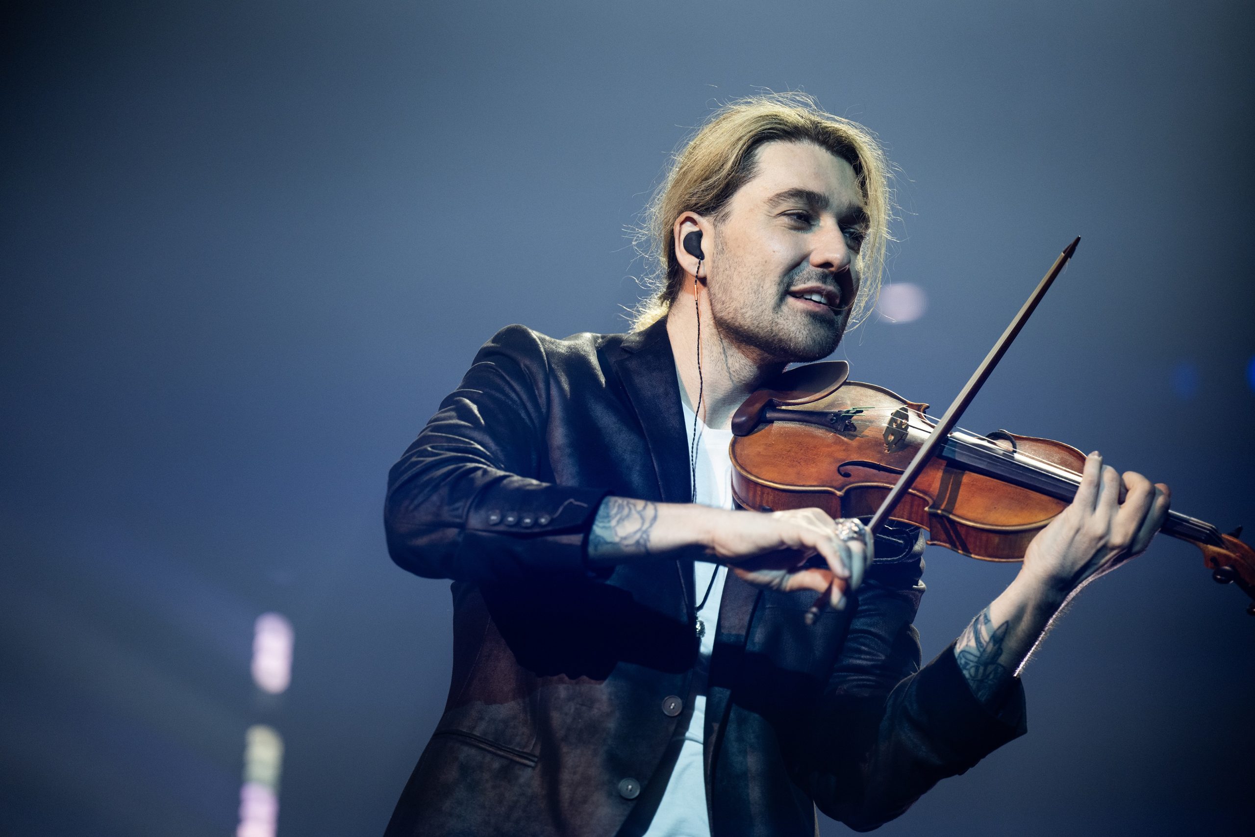 Violinist on stage in a black jacket playing a violin, focused on the performance.