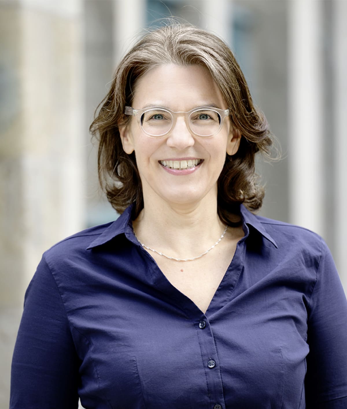 https___pondus-hpg.s3.eu-central-1.amazonaws.com_fischer_public_AjLlnLUcoESHGBlgjREO6CMex6OG6mehi11jarWttgf_AF_Bianca_20Walther_Vorschau - IN München - Das Stadtmagazin Smiling woman with short brown hair and clear glasses wearing a navy blue button‑front shirt outdoors.