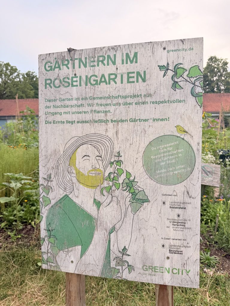 projekt-gärtnern-im-rosengarten-muenchen - IN München - Das Stadtmagazin Holzschild mit der Aufschrift "Gärtnern im Rosengarten" im Rosengarten München