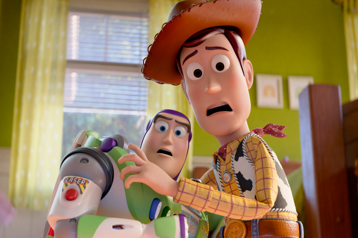 Woody and a purple-haired friend stare in alarm as they fix a green laser toy marked LASER in a sunny room.