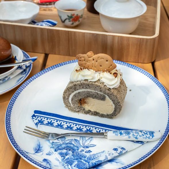 w=589 (6) - IN München - Das Stadtmagazin Slice of chocolate Swiss roll with cream filling and whipped cream topping, topped with two small cookies on a blue-and-white plate.