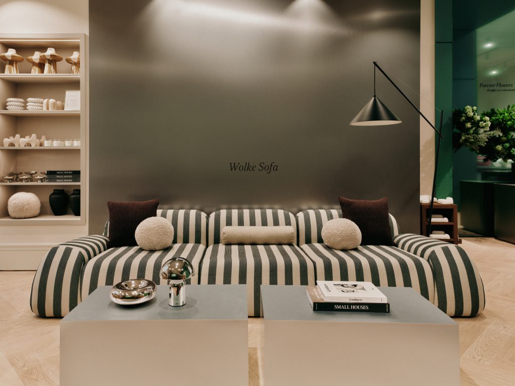 2026-07-BA-WESTWING-MUNICH-STORE-14-439 - IN München - Das Stadtmagazin Showroom scene with striped grey-and-white sofa, glass coffee tables, and metallic décor in a modern living room display
