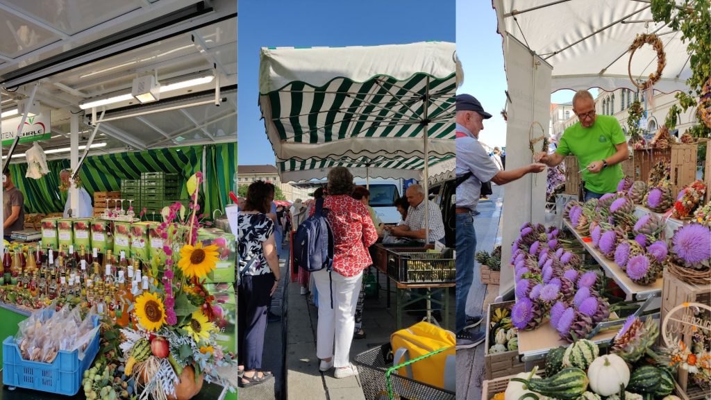 Bauernmarkmeile copyright BBV (2) - IN München - Das Stadtmagazin Market stall with bottled drinks and green juice cartons, sunflowers in the foreground under a canopy.