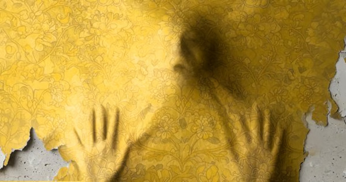 Shadow of a person pressing against a yellow floral wallpaper that’s peeling away from a wall.