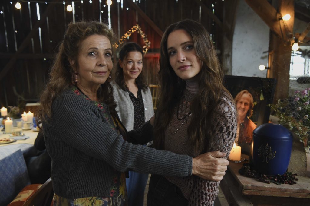 Three women posing together at a cozy, candlelit gathering in a rustic venue, smiling at the camera in the foreground.