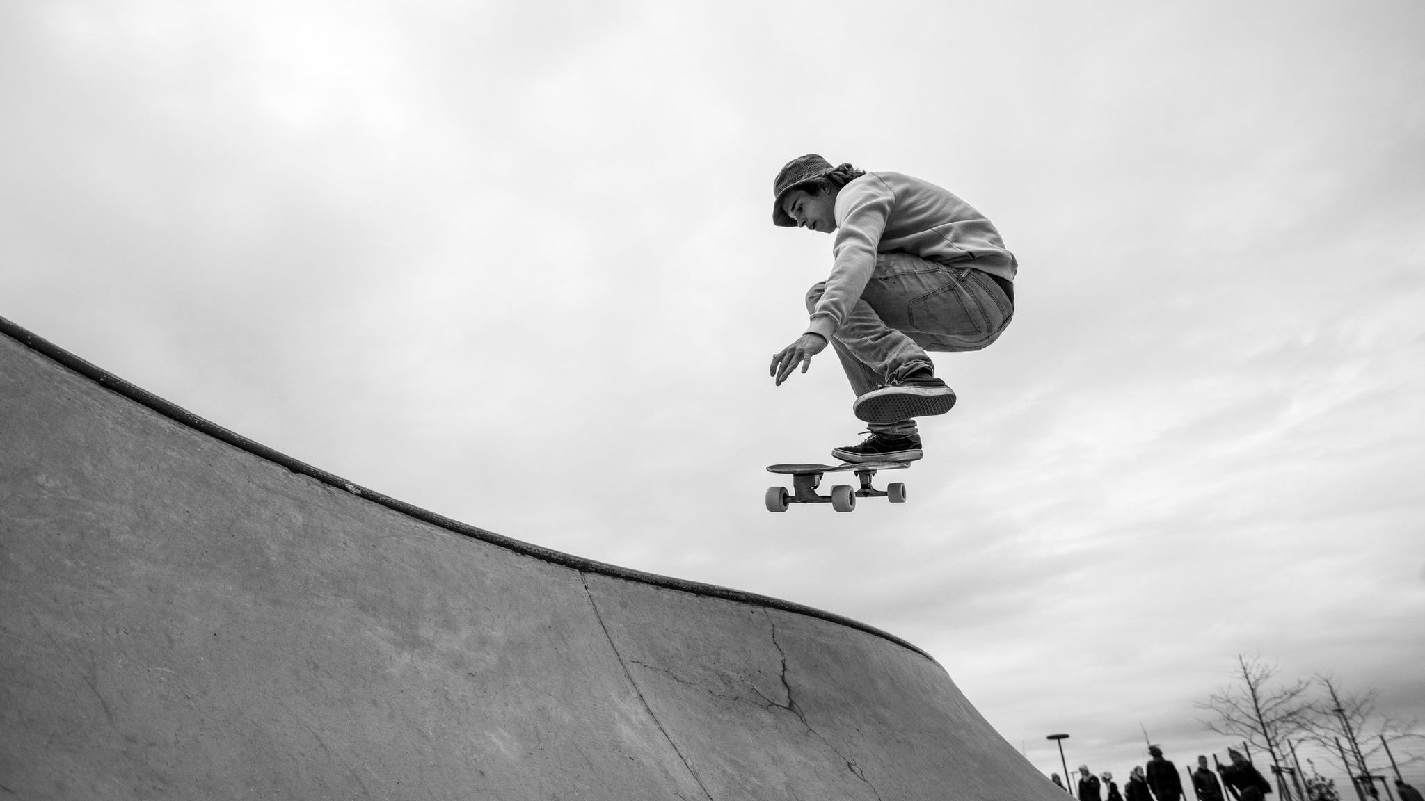 Feierwerk_Boom_Skate-Action_Credits_Olf_Olszewsky - IN München - Das Stadtmagazin Skateboarder performing a mid-air trick on a curved ramp, wearing a beanie and hoodie, in black-and-white.
