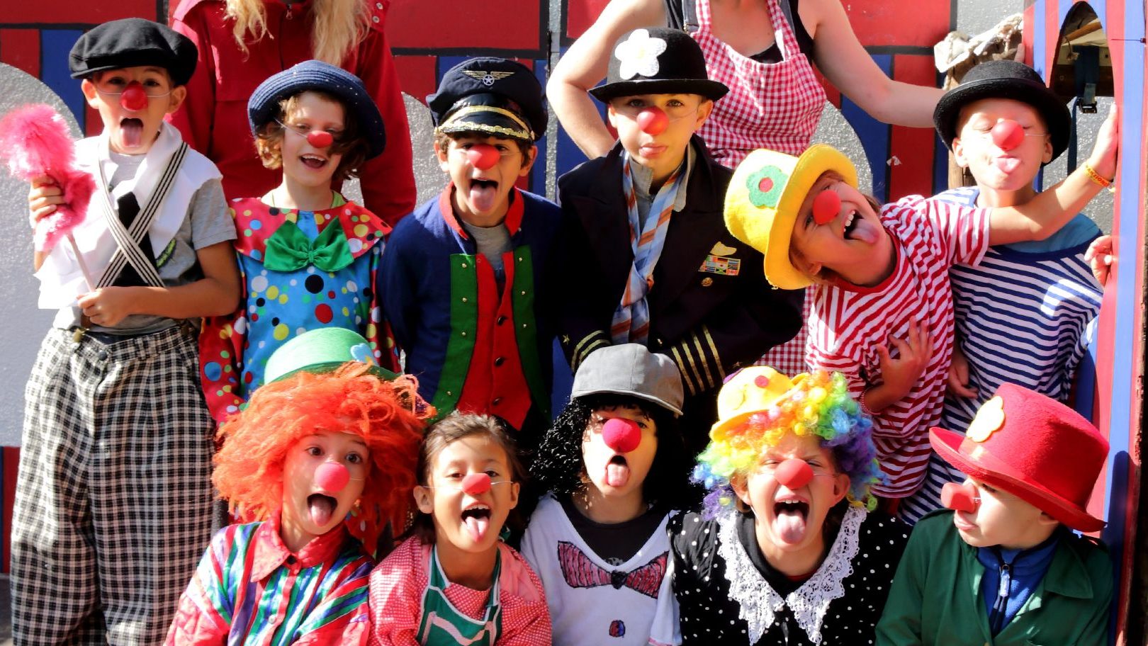 KIZA_Alt3 - IN München - Das Stadtmagazin Group of kids dressed as clowns posing for a photo at a colorful event, all with red noses and playful outfits.