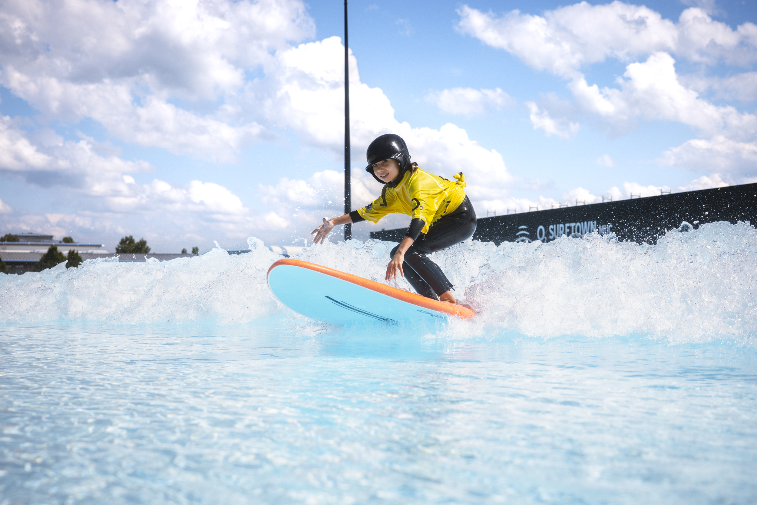 Maedchen mit Helm surft auf einer artifiziellen Welle im O2 Surftown Much