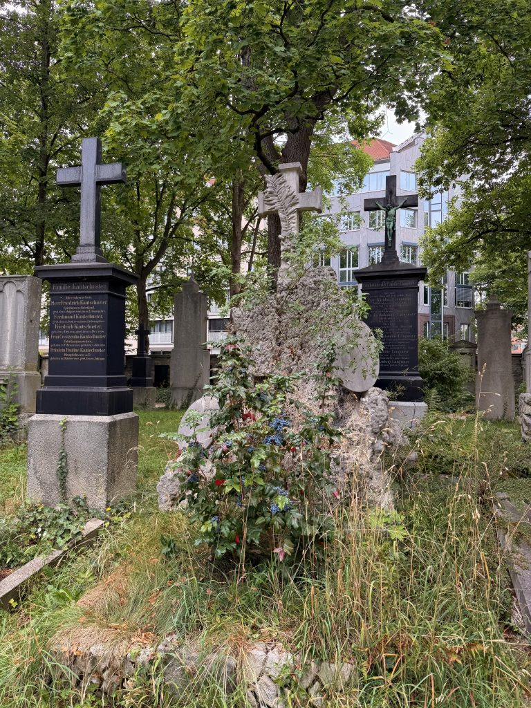 Grab aus Tuffstein, zwischen weiteren Gräbern, im Hintergrund Wohnhäuser