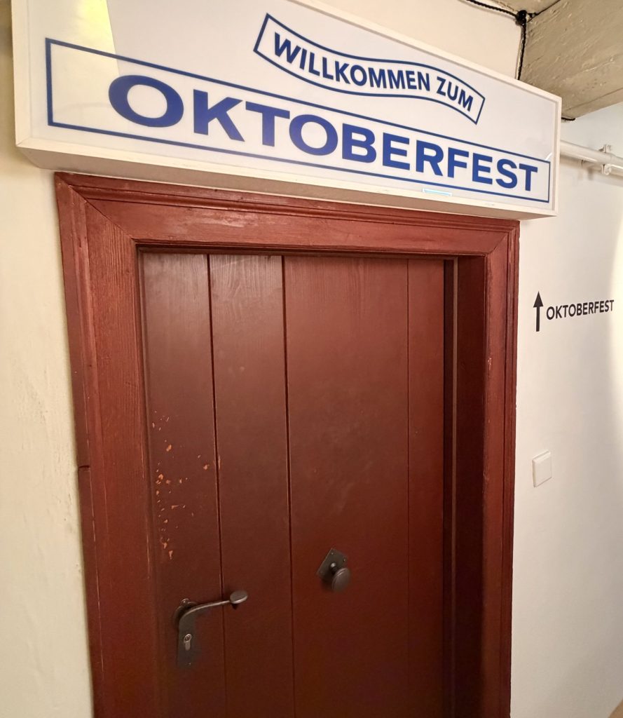 biermuseum-muenchen-oktoberfestmuseum-eingang - IN München - Das Stadtmagazin Schild'WILLKOMMEN ZUM OKTOBERFEST' mit blauer Schrift über einer Holztür