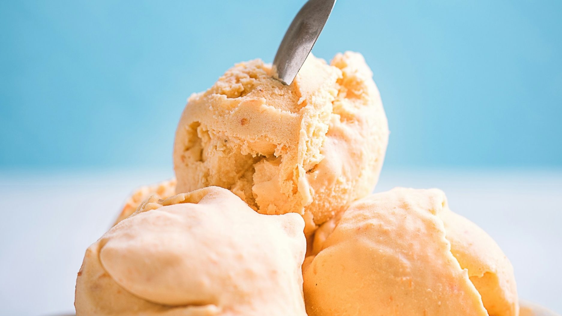 gelato-sommerferienprogramm - IN München - Das Stadtmagazin Close-up of peach-colored ice cream scoops with a spoon embedded in one, stacked against a blue background.