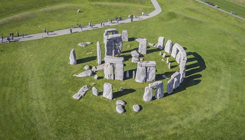Stonehenge - IN München - Das Stadtmagazin A Stonehenge-like stone circle on a grassy field with tourists walking along a curved path nearby.