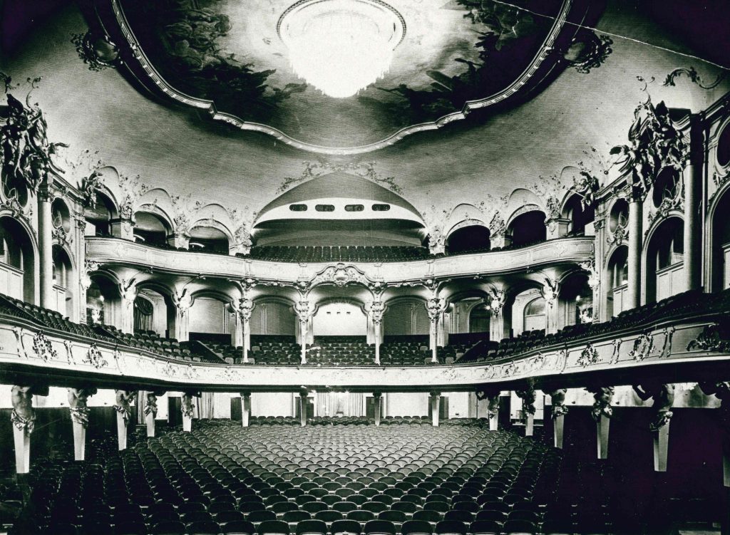 1939 nach dem Umbau_erstmals schräge und feste Reihengestaltung - IN München - Das Stadtmagazin Interior of an ornate historic theater with multiple curved balconies and gilded decorations, rows of seats facing the stage (black-and-white photograph).