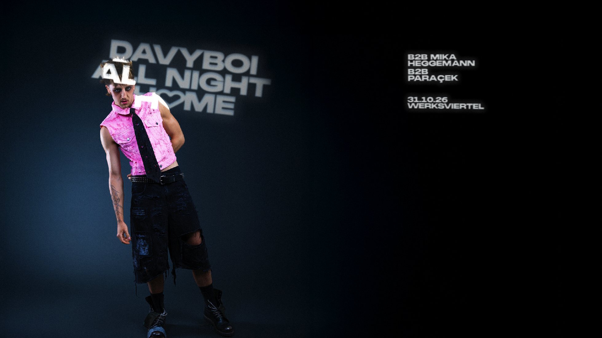 DNA - IN München - Das Stadtmagazin Male model in a pink sleeveless shirt and black tie posing against a dark backdrop with promotional text on the left side of the image.