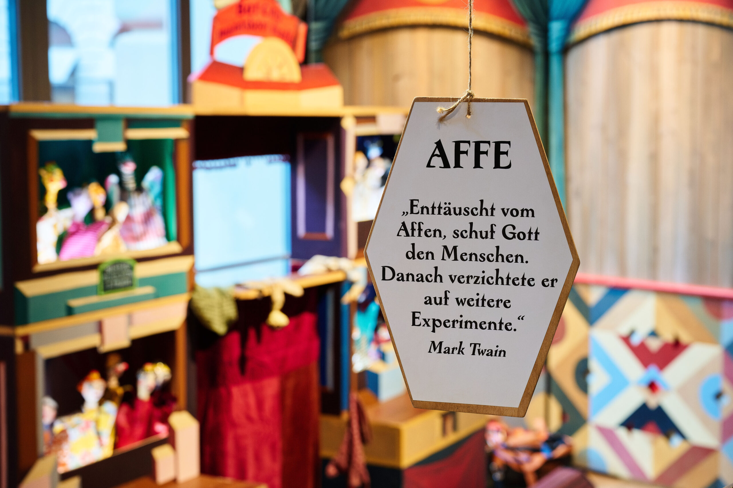 Hanging hexagonal sign reading 'AFFE' with a German quote in a colorful toy store backdrop.