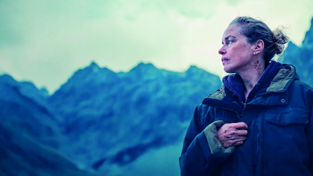 FILMTIPP Die andere seite - IN München - Das Stadtmagazin Woman in a blue winter jacket gazes to the right with a rugged mountain range in the misty background.