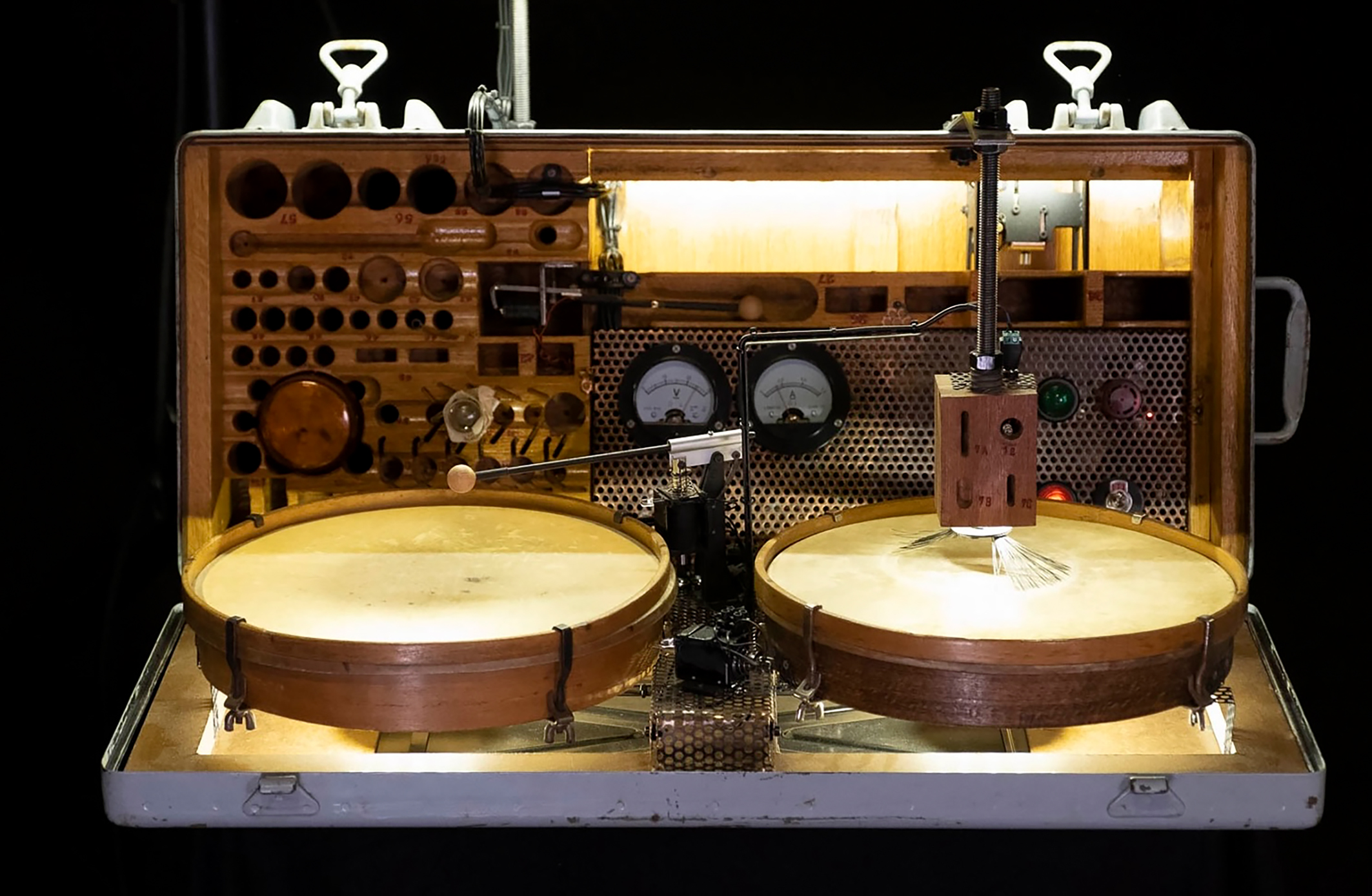 Vintage laboratory device with two large wooden drums, analog gauges, and a perforated metal panel behind glass doors