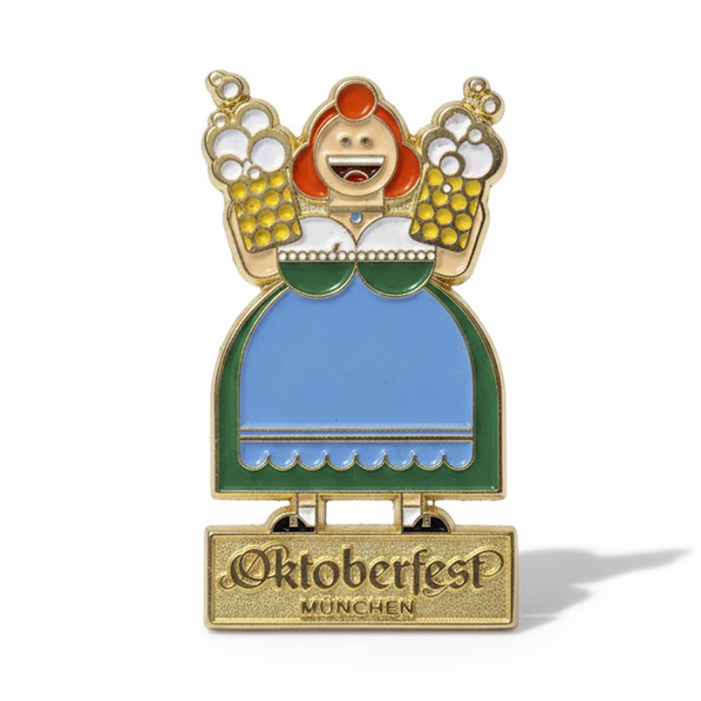 Decorative Oktoberfest enamel pin featuring a smiling woman in traditional dress holding two beer steins, with 'Oktoberfest München' inscription on the base.