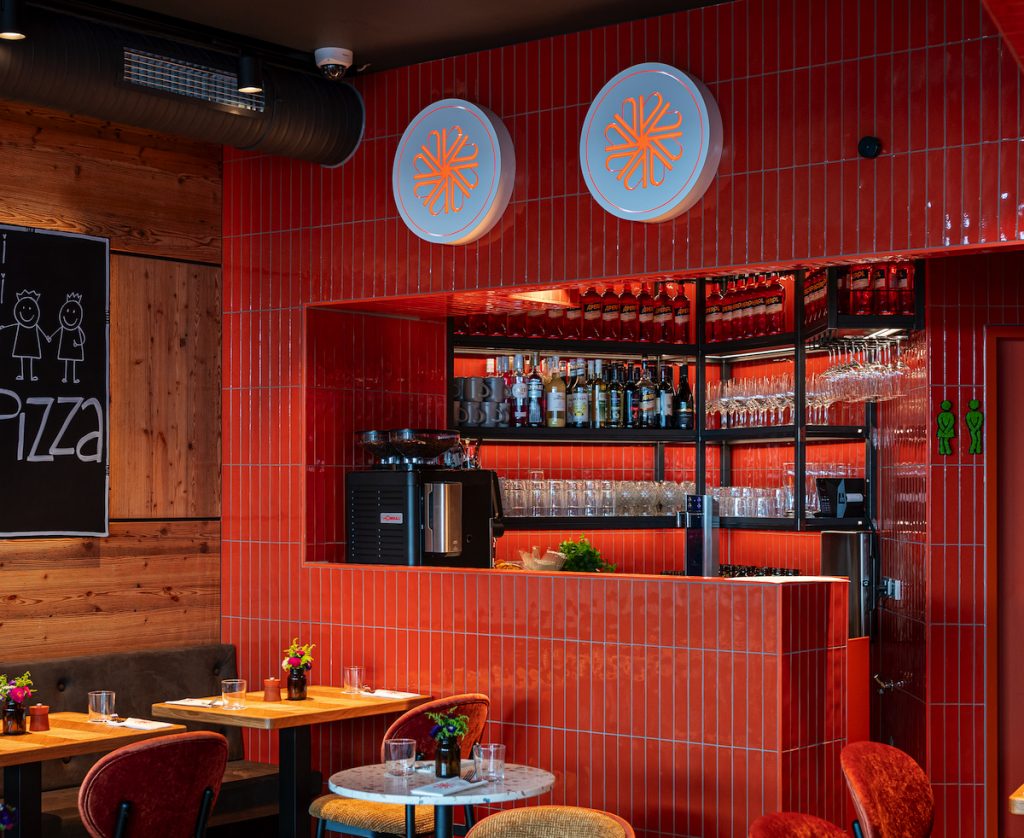 Bar interior with orange tiled wall and backlit shelves of bottles and glassware behind the counter