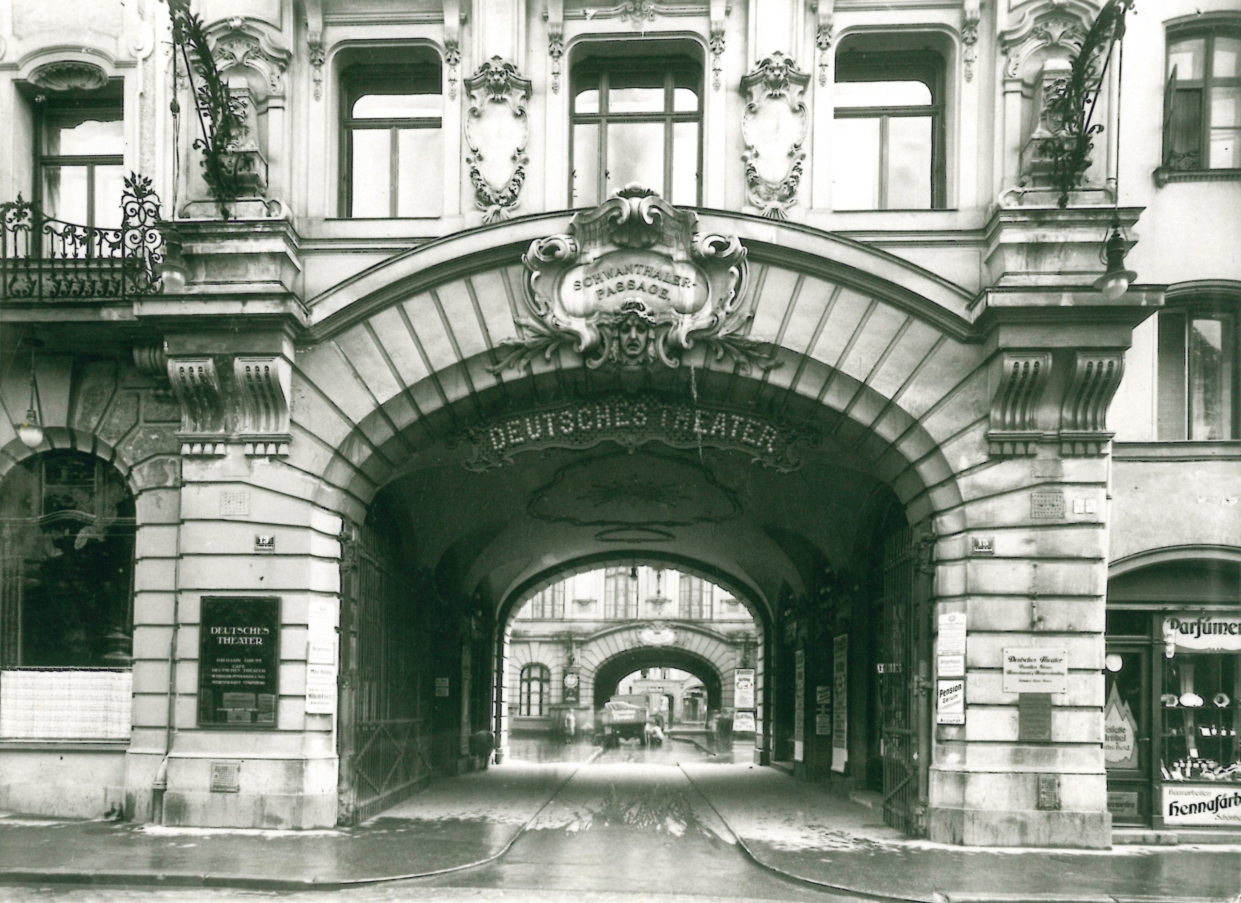 Torbogen 1930 © Stadtarchiv München - IN München - Das Stadtmagazin Facade of an ornate European building with a large arched entrance and decorative plasterwork; sign reads Deutsches Theater above the arch.