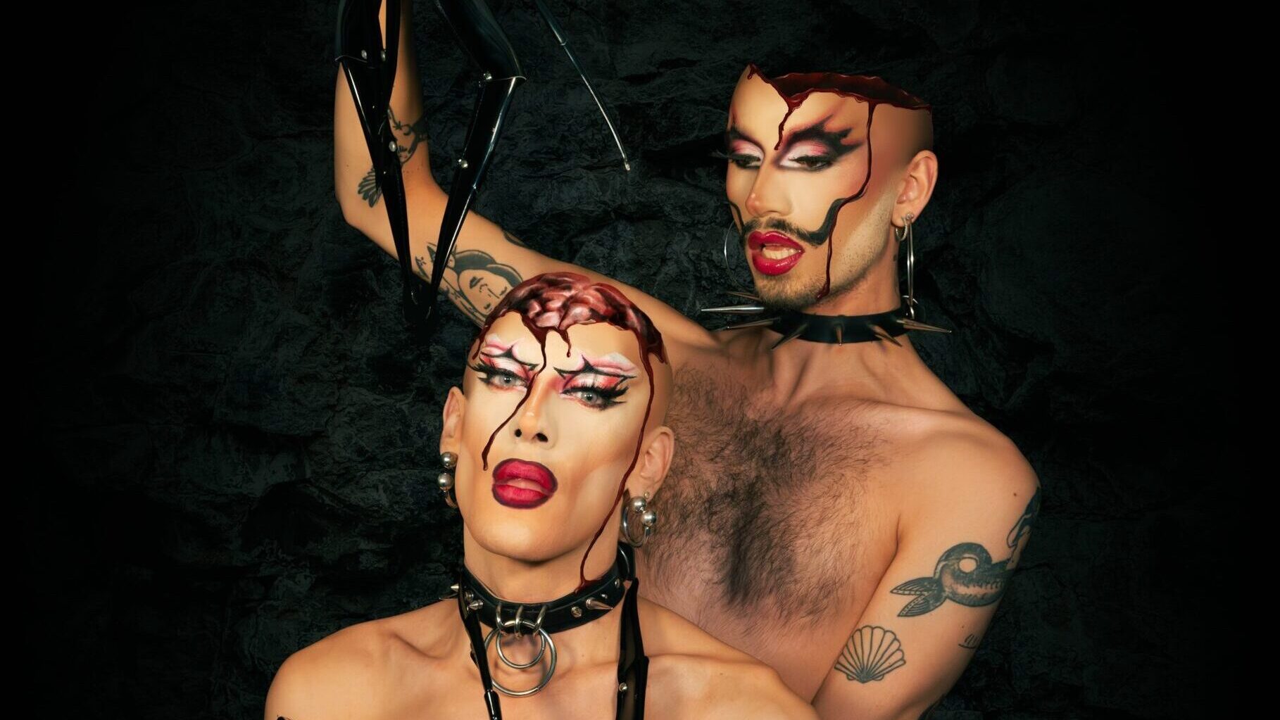 Wigz_Halloween_Special_Milla_Club - IN München - Das Stadtmagazin Two drag performers with dramatic makeup and bondage-inspired accessories pose shirtless against a dark textured background.