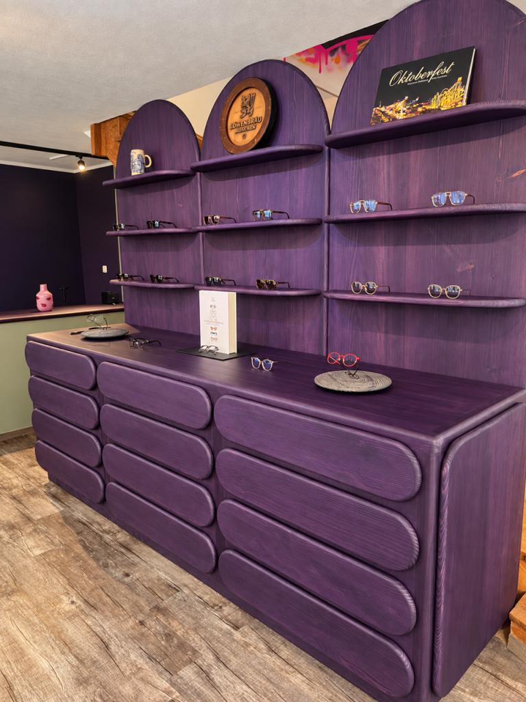 image0Baumanis - IN München - Das Stadtmagazin Purple wood display counter and shelves showcasing sunglasses in a boutique eyewear shop.