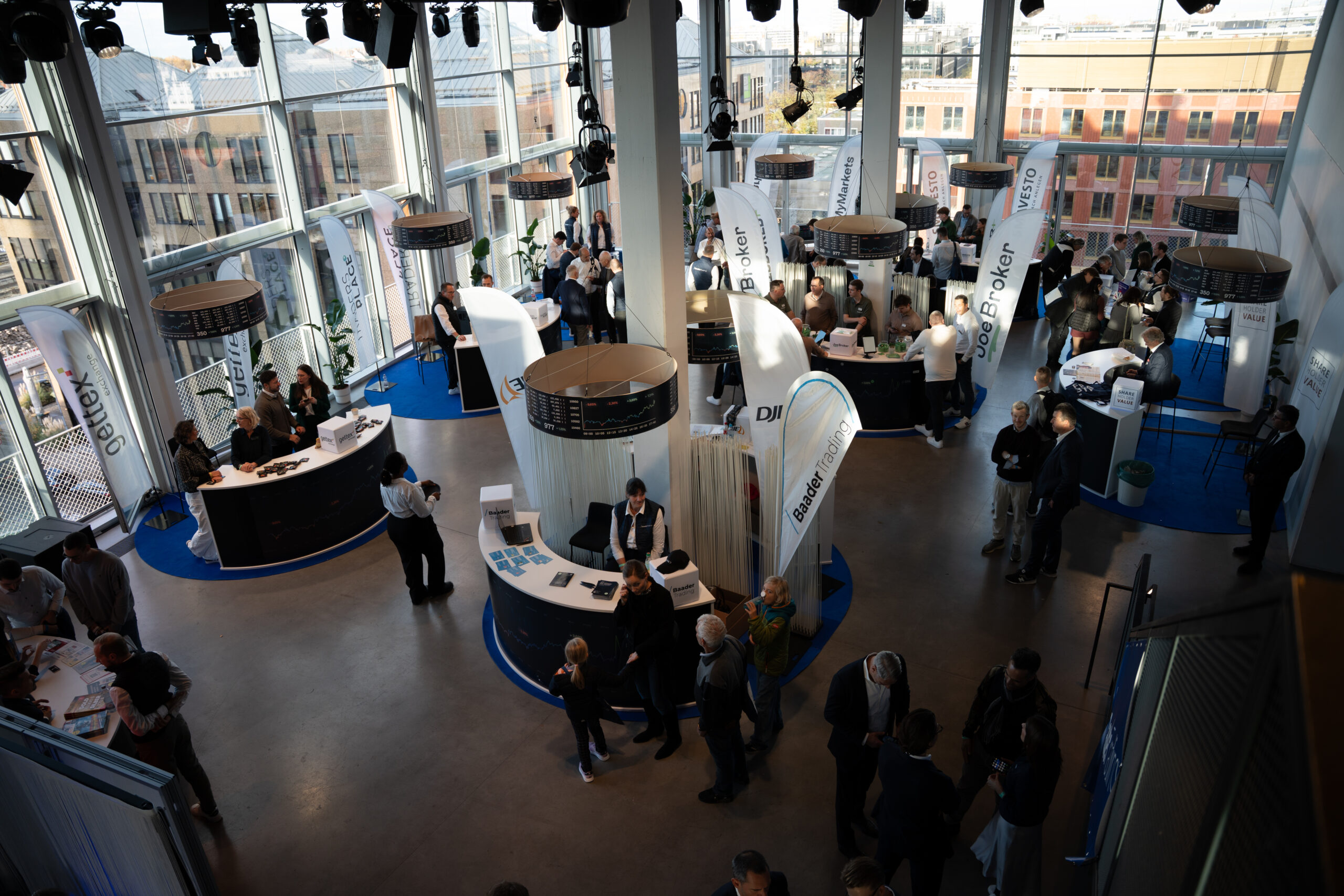 A7_00191 - IN München - Das Stadtmagazin Crowded exhibition hall with multiple booths, tall white banners, and people networking.
