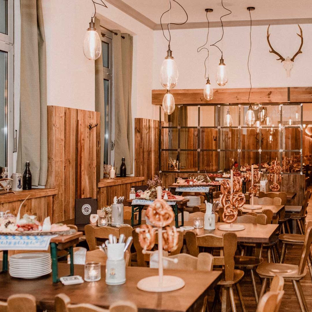 Rustic restaurant interior with wooden panel walls, warm pendant lights, and pretzel centerpieces on tables.