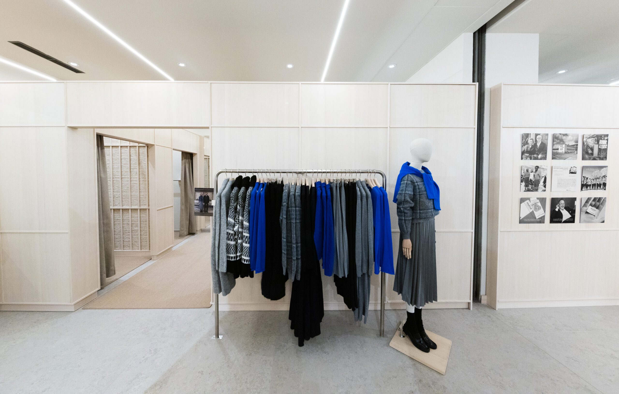 MAERZ_Muenchen_store_MUC_07 - IN München - Das Stadtmagazin Mannequin wearing a gray coat and blue scarf beside a rack of blue and gray coats in a minimalist showroom. Note: plain, well-lit retail display with a clothing rack and mannequin.