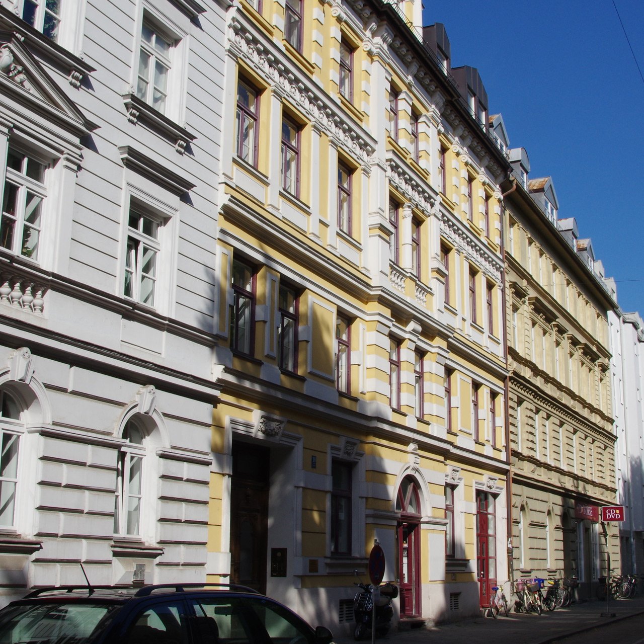 Colorful historic row houses with ornate white and yellow facades along a sunny street.