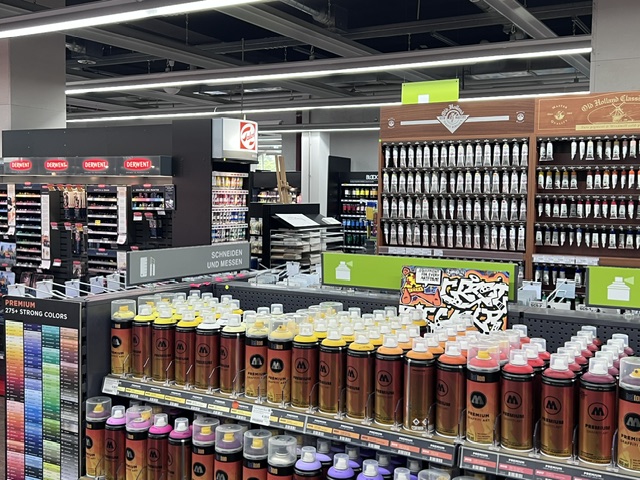 Gerstäcker München - IN München - Das Stadtmagazin Row of brown spray bottles with white caps lined up on a store shelf in a wide retail aisle behind them are more product displays and shelves.